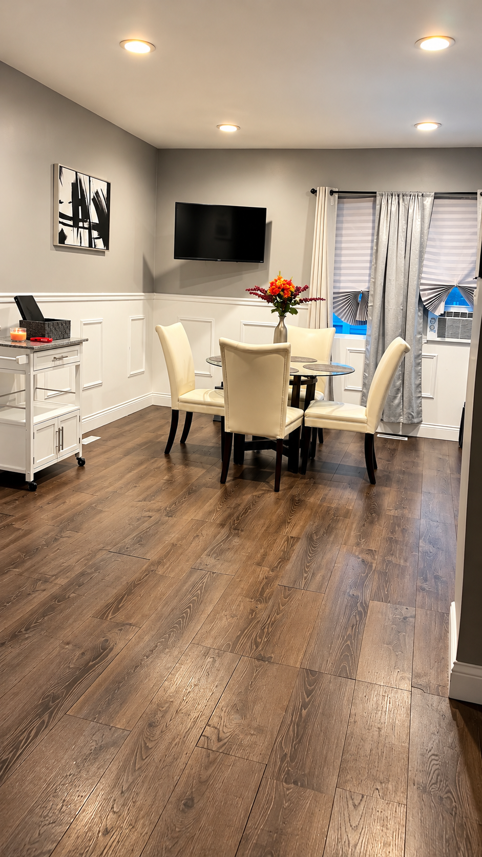Dining area — round glass table, wainscoting, wall-mounted TV
